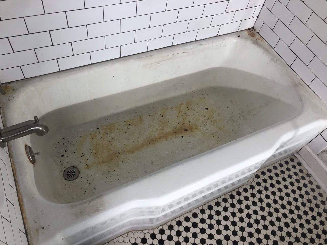 A dirty bathtub with rust stains on it.